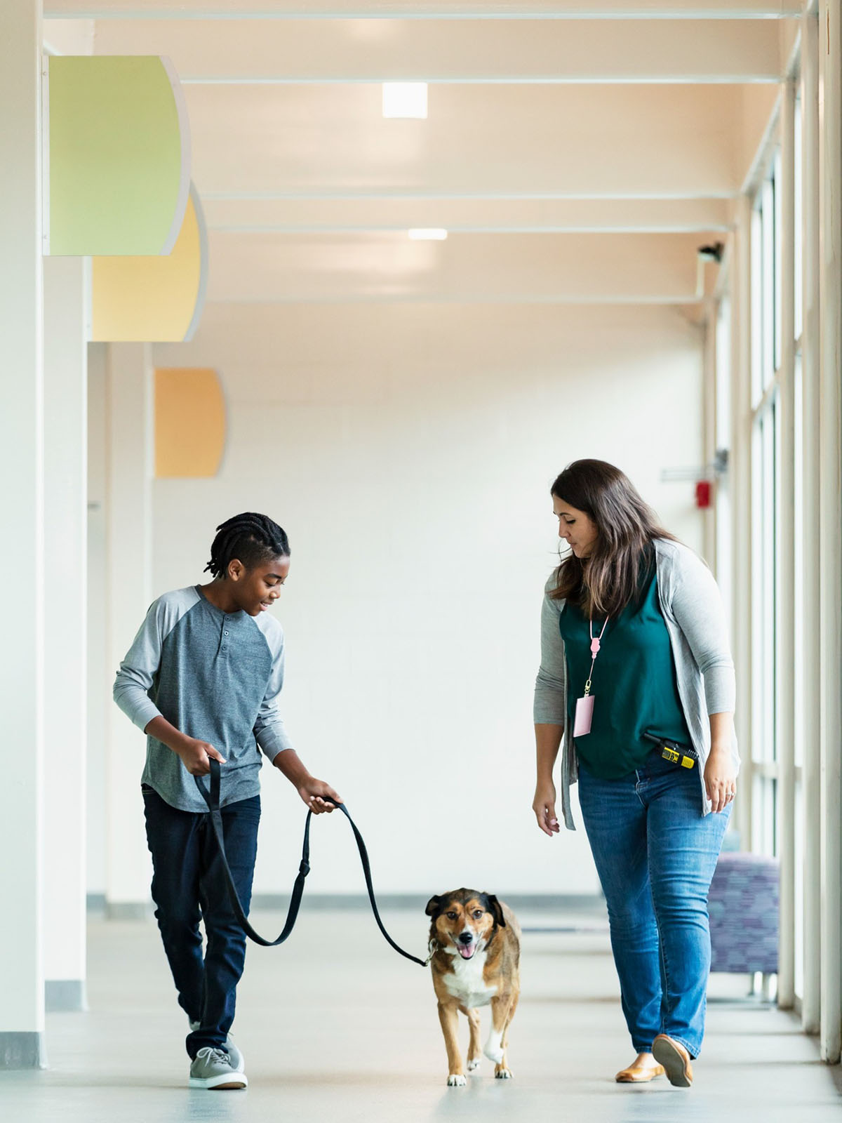 two individuals walking a dog down a bright corridor