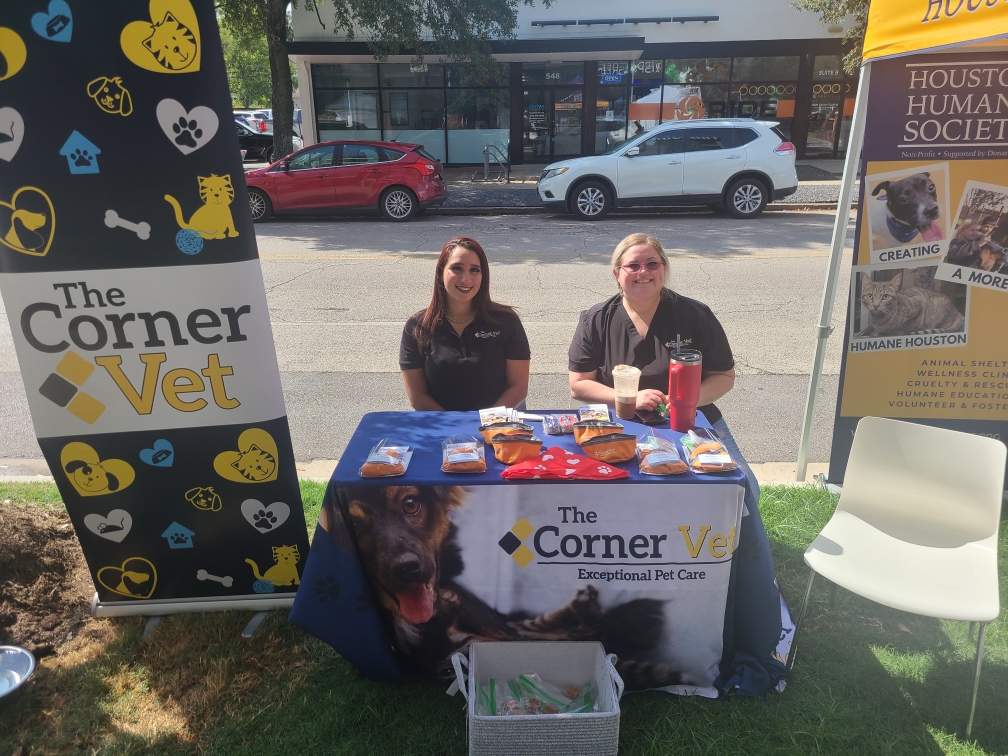 two people sitting at 'The Corner Vet' informational booth with pet care materials on the table